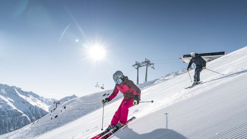 Ausflugsziele in Sölden gesucht? Zwei Skifahrer fahren bei sonnigem Wetter den schneebedeckten Hang hinunter