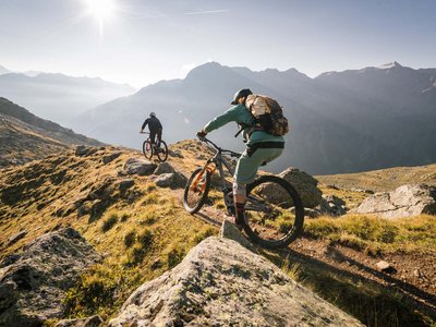 Ausflugsziele in Sölden gesucht? Zwei Mountainbiker fahren einen Bergpfad in den Alpen bei Sonnenschein hinab
