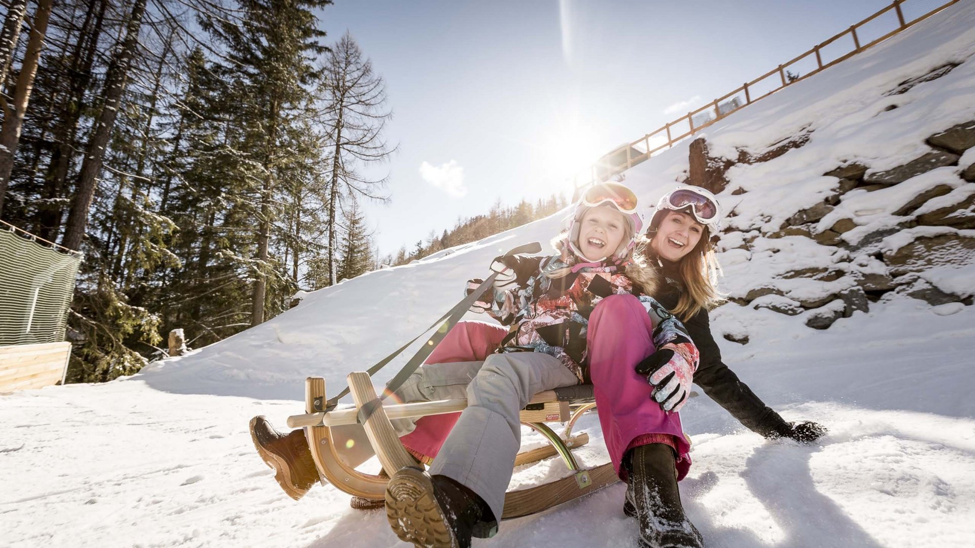 Ausflugsziele in Sölden gesucht? Frau und Kind lachen beim Rodeln im Schnee an sonnigem Wintertag