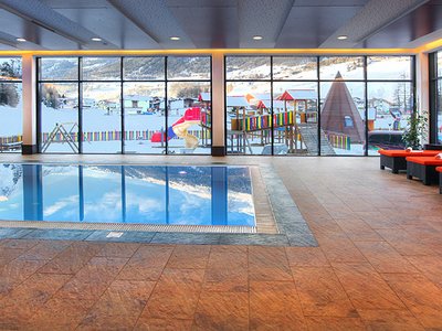 Wellnesshotel in Sölden: Hotel Sunny Innenpool mit roten Liegestühlen und Blick auf verschneiten Spielplatz draußen