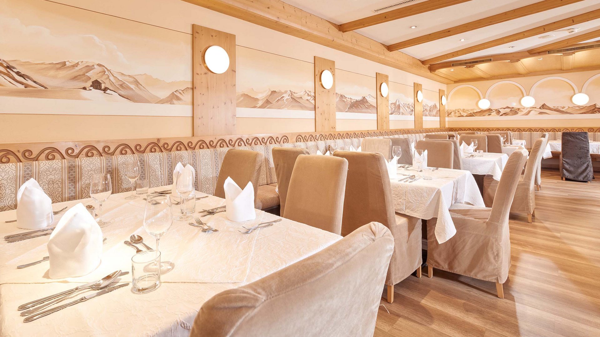 Hotel in Sölden mit 4-Sterne-Service Heller Speisesaal mit gedeckten Tischen und Berglandschaft an den Wänden