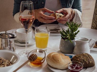 Dein 4-Sterne-Hotel im Ötztal Person hält Croissant bei einem Frühstückstisch mit Saft und Kaffee