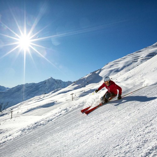 Skiing holiday in Sölden? Come to Hotel Sunny! Skier skiing down a snowy slope under bright sun and clear blue sky