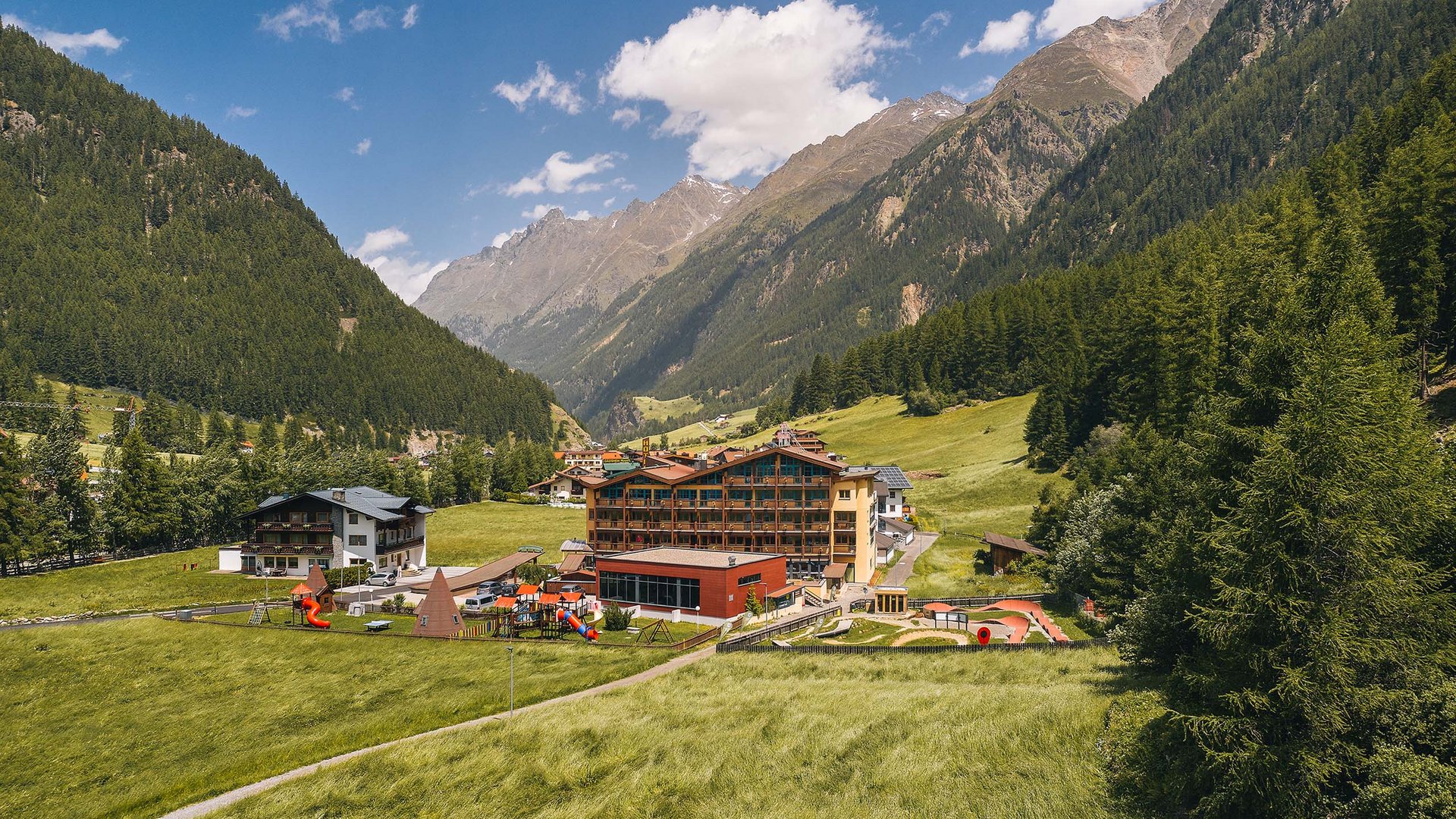 Dein 4-Sterne-Hotel im Ötztal Bergdorf mit Hotel und Spielplatz in einem grünen Tal unter blauem Himmel