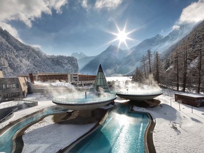 Family hotel in Sölden: Hotel Sunny Sölden Thermal pools emitting steam in snowy alpine landscape under bright sun