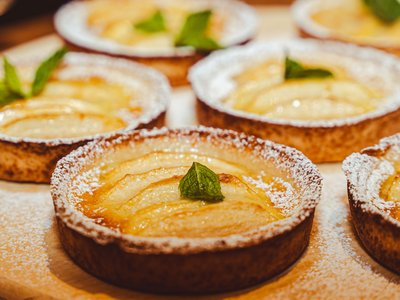 Dein 4-Sterne-Hotel im Ötztal Mehrere Birnen-Törtchen mit Puderzucker und Minzblatt auf einem Holzbrett