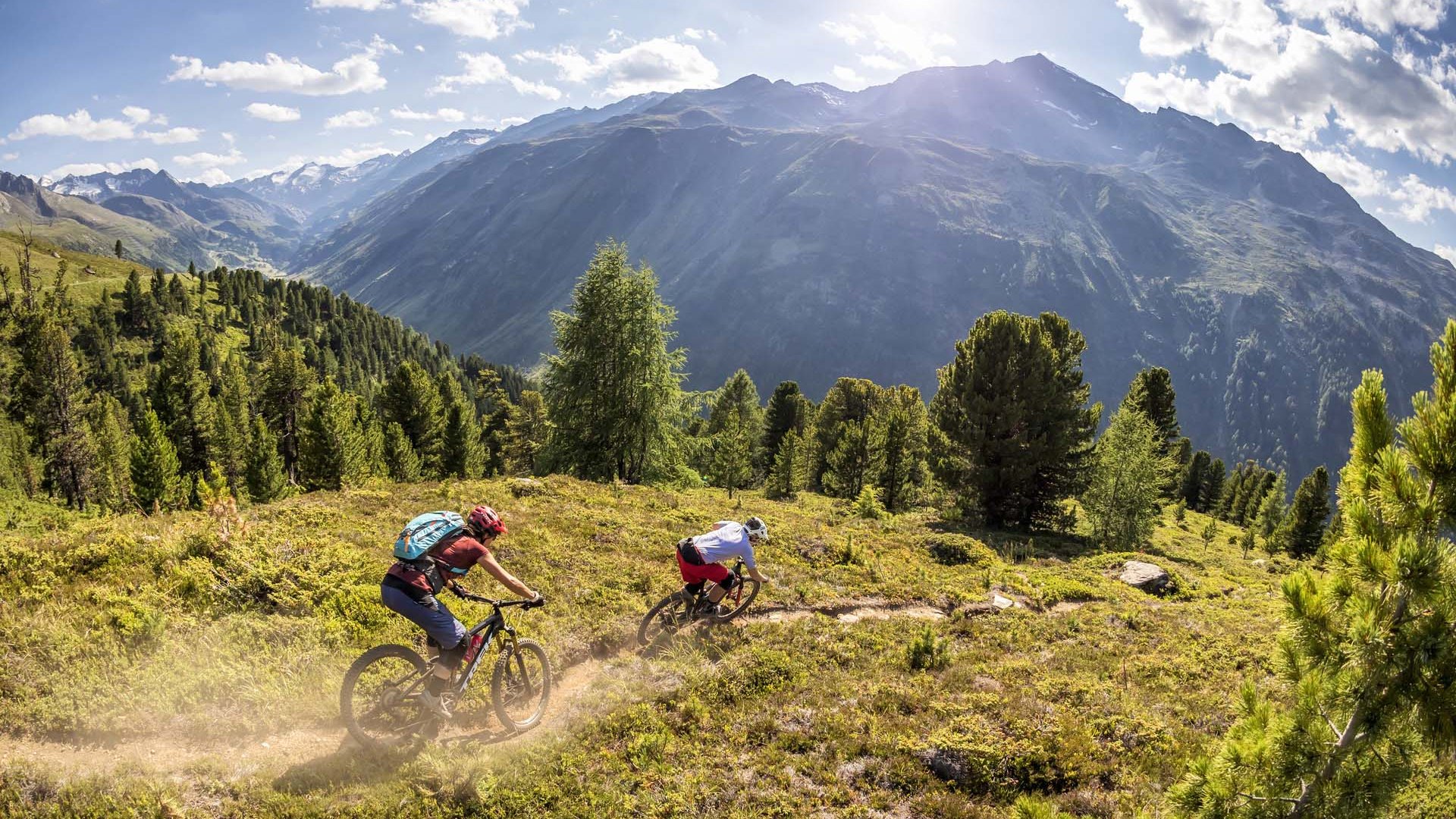 Bikehotel in Sölden: Hotel Sunny Zwei Mountainbiker fahren einen Waldweg in den Bergen bei sonnigem Wetter
