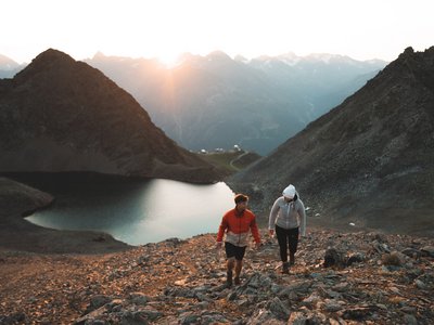 Ausflugsziele in Sölden gesucht? Zwei Wanderer steigen an einem Bergsee vor alpiner Bergkulisse auf